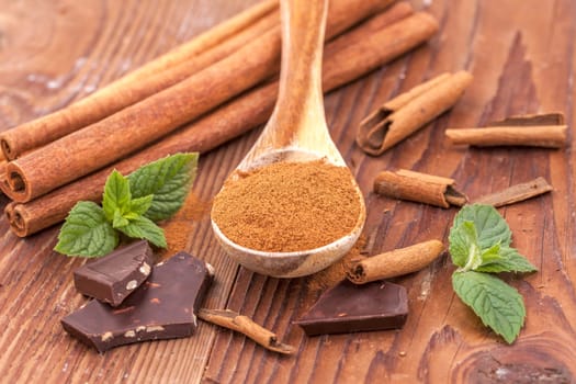 Cinnamon powder on a wooden spoon, mint leaves, cinnamon sticks, and chunks of dark chocolate.