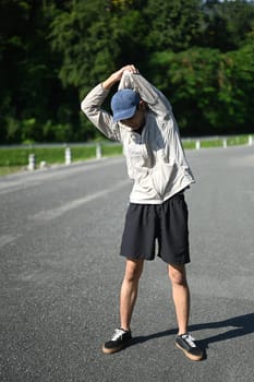 Full length man athlete warming up for an outdoor workout in a serene park.