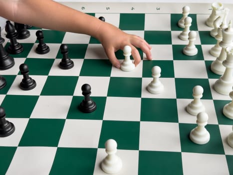 Childs hand moving chess piece on green and white chessboard with black and white pieces.