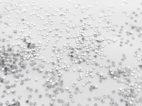Shimmering silver star confetti on white background for festive occasions.