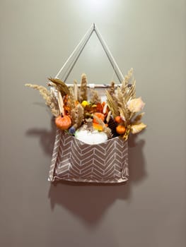Autumn wall hanging with pumpkins, gourds, and dried foliage on neutral background.