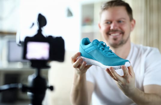 Close-up of smiling middle-aged man filming red sneaker on camera and tell in vlog. Male describing quality of new boots on display of digital device. Technology and blogger concept