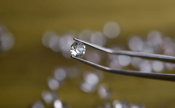 Close-up of beautiful shining crystal. Macro shot of luxury round white diamond in tweezers. Big carat size. Jeweler checking polished brilliant. Precious stone concept