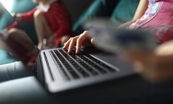 Close-up of person working on laptop sitting on sofa. Young woman typing on grey modern gadget. Freelancer on quarantine period. Technology and remote job concept