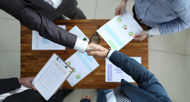 Top view of business team shaking hands. Conference room with executive manager accountant and employee. Good deal and financial report. Papers with charts on wooden table