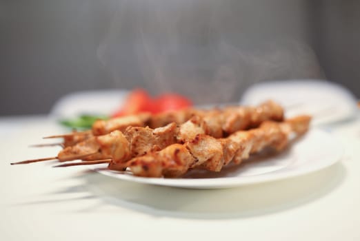 Close-up of delicious grilled chicken pieces on bamboo skewers on white plate. Aromatic meat for dinner. Home barbeque. Tasty meal and healthy food concept