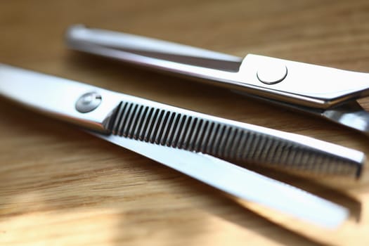 Close-up of two pairs of scissors for cutting and thinning out hair. Professional hairdresser instruments for work. Metal equipment laying on wooden table