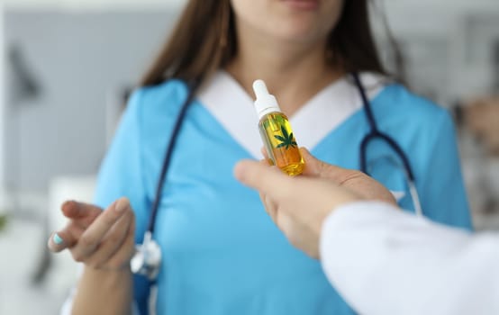 Close-up of male hands giving bottle of cannabinoid oil to doctor. Female person in medical uniform with stethoscope. Pain medication. Healthcare and medical marihuana concept
