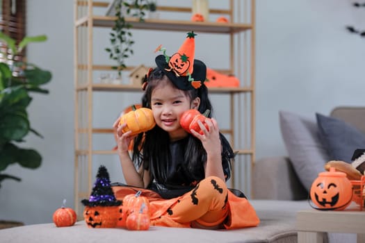 Cute little girl wearing a Halloween costume holding a pumpkin at home with happy eyes. looking at the camera..