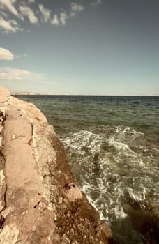 Seascape with a view of the rocky coast, beautiful sea surface, waves crashing on a rocky cliff. A clear sunny day.