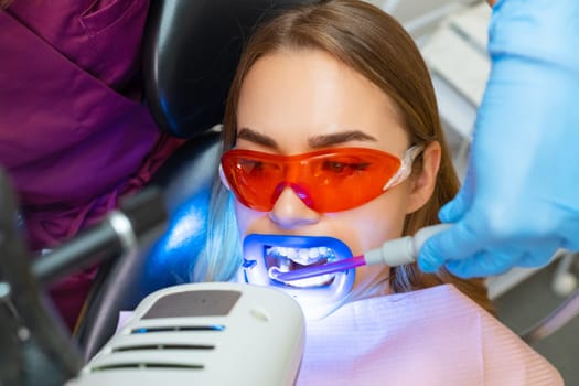 Aspiration of fluid from the oral cavity during the teeth whitening procedure for woman patient at dental clinic