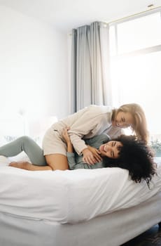 Happy, laughing and a lesbian couple in the bedroom in the morning for love and bonding. House, romance and gay or lgbt women on a bed for conversation, tickle and comfortable in home together.