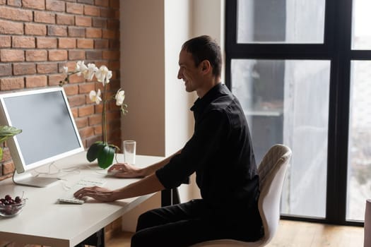 Focused young man using laptop, typing on keyboard, writing email or message, chatting, shopping, successful freelancer working online on computer