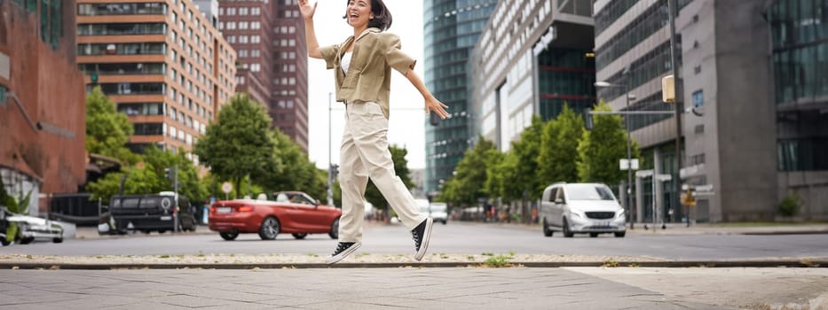 Portrait of asian happy girl jumping and dancing in city centre, posing on streets, express joy and excitement. Copy space