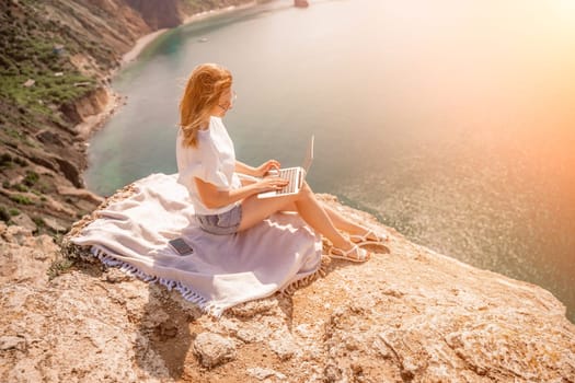 Freelance woman working on a laptop by the sea, typing away on the keyboard while enjoying the beautiful view, highlighting the idea of remote work