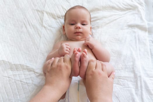 Baby's legs lifted gently as mother's touch soothes. Concept of alleviating constipation in infants