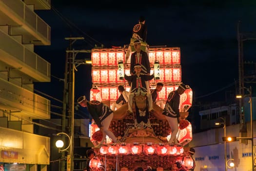 Kishiwada, Japan - September 17, 2023: Young men with lanterns and traditional clothing atop portable shrine at night festival. High quality photo