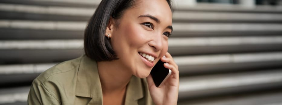 Communication. Young asian woman talking on mobile phone, having a telephone call, using smartphone while sitting on street.