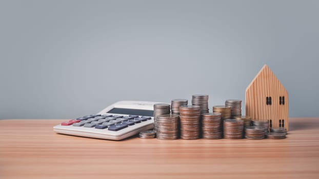 Model wooden house, calculator and coins lined up on wooden floor on white background. Concepts of finance, savings and investment. Real estate concepts.