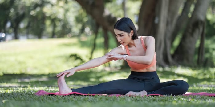 Attractive and charming Asian woman in her 30s in sportswear doing yoga poses, relaxing muscles. Asian woman practicing yoga in a beautiful green park.