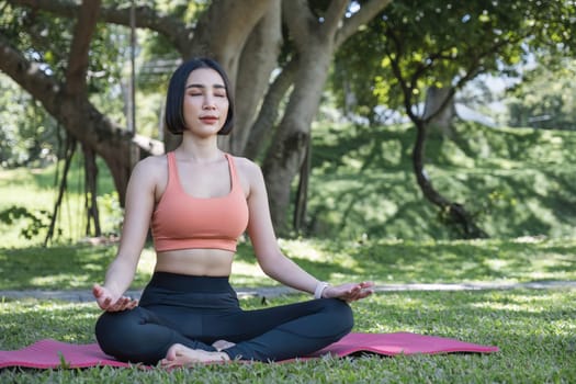 Attractive and charming Asian woman in her 30s in sportswear doing yoga poses, relaxing muscles. Asian woman practicing yoga in a beautiful green park.