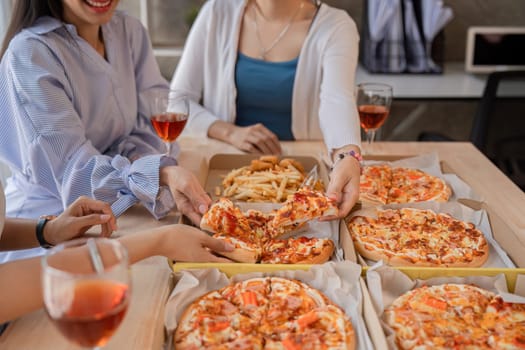 Group of Asian friends together to celebrate Christmas with champagne and eating pizza at home. Joy of holiday party with friends or colleague concept.