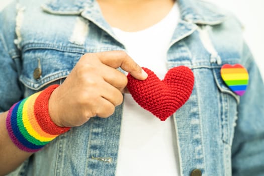 Asian lady wearing rainbow flag wristbands and hold red heart, symbol of LGBT pride month celebrate annual in June social of gay, lesbian, bisexual, transgender, human rights.