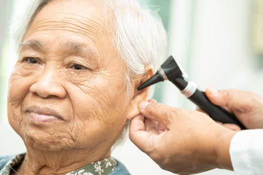 Audiologist or ENT doctor use otoscope checking ear of asian senior woman patient treating hearing loss problem.