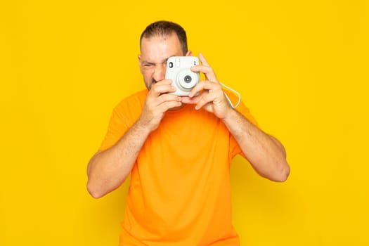 Bearded Hispanic man in his 40s taking a photo with an instant camera, isolated on yellow background