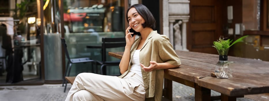 Young woman having conversation on mobile phone, sitting outdoors and making phone call, using smartphone, talking.