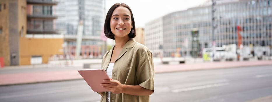 Portrait of young stylish woman walking with tablet, going somewhere in city.