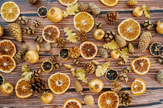 Pieces of dried oranges, pomegranates, pine cones, oak leaves lie on a wooden background. Top view. High quality photo