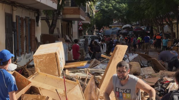 Residents in Benetuser, Valencia, clean streets and clear debris after a DANA storm flood, with wrecked cars visible on Nov 2, 2024,
