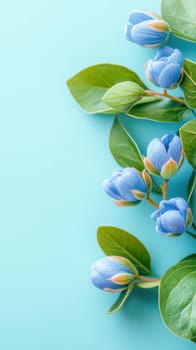 Beautiful arrangement of blue flower buds and green leaves creates a natural border on a light blue background