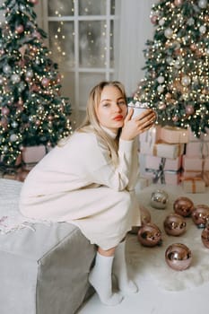 Blonde in a bright Christmas interior with a cup of hot drink with marshmallows. New Year's interior in pink tones. The winter holidays period.