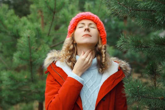 Sick exhausted young woman suffering from acute sore in throat flu, touches her neck with hand, she feels bad outdoors in winter park
