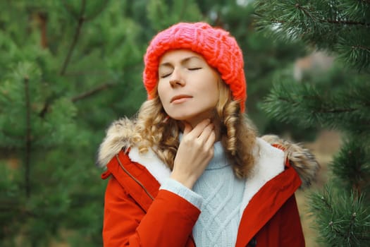 Sick exhausted young woman suffering from acute sore in throat flu, touches her neck with hand, she feels bad outdoors in winter park