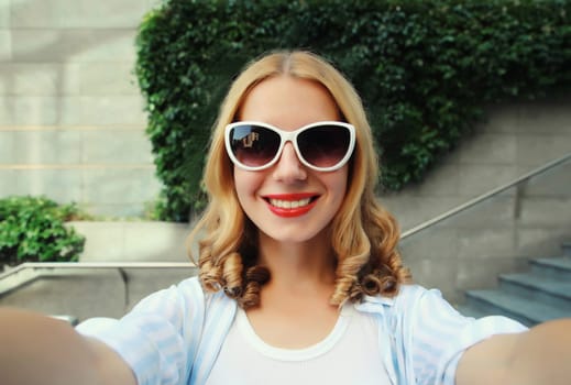 Summer close up portrait of happy cheerful smiling young woman taking selfie with phone, joyful girl using smartphone against plant background on city street