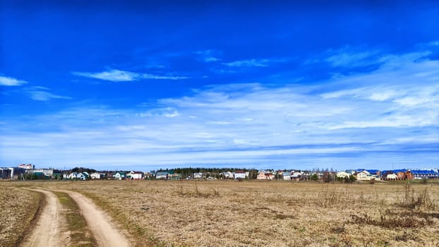A vast field of dry yellow grass stretches towards a picturesque village, framed by a bright blue autumn sky