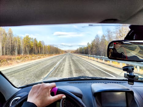 Car salon, windshield, hand of woman on steering wheel and landscape. View from seat of driver on nature landscape. Single trip of female traveler