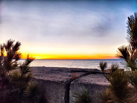 A stunning sunset casts vibrant colors over the ocean while rocky edges and greenery provide a natural frame to the view.
