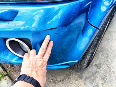 A person is seen pointing at a noticeable scratch on a bluecolored cars exterior, drawing attention to the damaged area