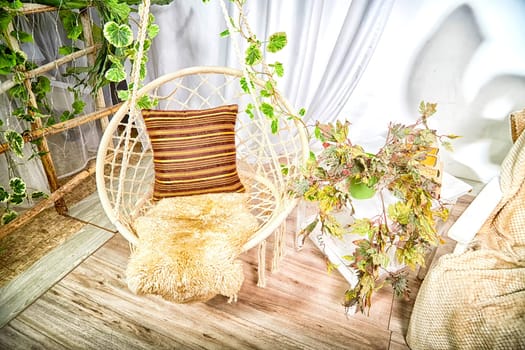 Modern cozy beautiful room with a braided rope macrame swing, chair, green plants, small table and curtains. Interior and background. Location for photo shooting