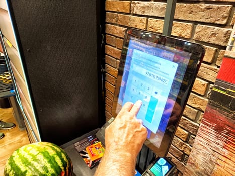 Kirov, Russia - September 15, 2024: A shopper interacts with a self-service checkout kiosk, scanning items and making a payment at a grocery store.