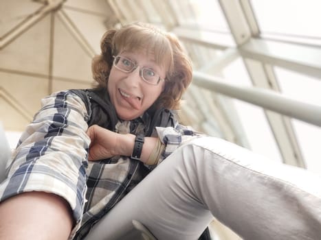 A woman in her middle ages takes a cheerful selfie in a busy airport hall while waiting for her flight. Her playful expression reflects her excitement for upcoming travels.