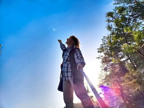 Happy female blonde tourist singing and taking selfie picture with smart mobile phone outside. Middle aged woman having fun on adventure nature trip in mountains
