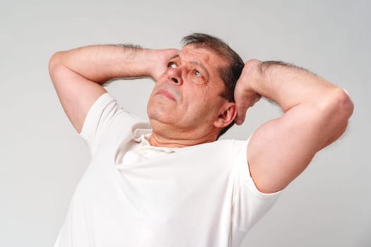 Elderly man stretching and relaxing indoors with a thoughtful expression and neutral background close up