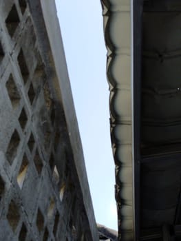 Close-up view of modern architectural elements featuring concrete lattice and metal roofing, showcasing urban design textures and patterns against a clear sky.