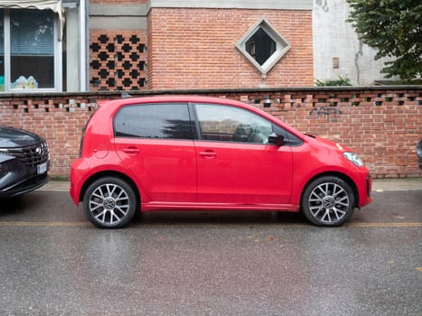 Cremona, Lombardy, Italy October 15th 2024 Bright red volkswagen up. gti parked on the street in front of a brick wall on a rainy day