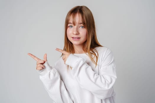 Young girl happily pointing against a neutral background while wearing a cozy white sweatshirt close up